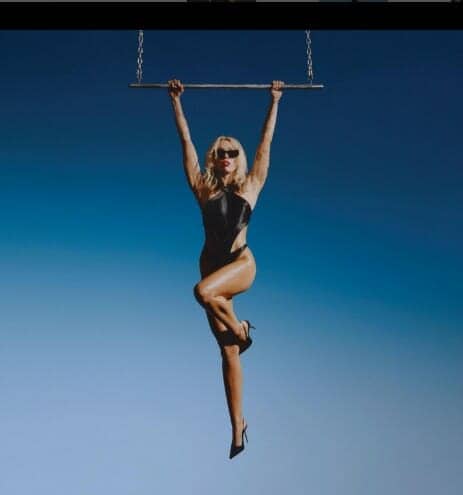 مايلي معلقة في الهواء ممسكة بأرجوحة على خلفية زرقاء ساطعة