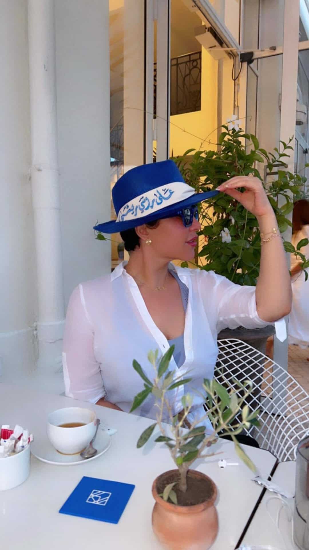 ظهرت شمس الكويتية مرتدية شيميز أبيض شفافاً مفتوح الصدر، وبونيه أزرق ملفوفاً بوشاح أبيض كتب عليه: "على راسي ريشة"